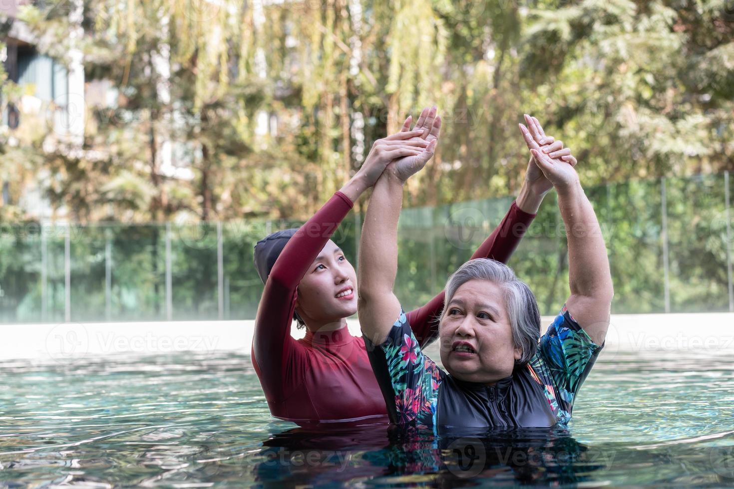 Young trainer helping senior woman in aqua aerobics and working out in the pool. old woman and mature man doing aqua aerobics exercise in swimming pool, Elderly sports, and active lifestyle concept. photo