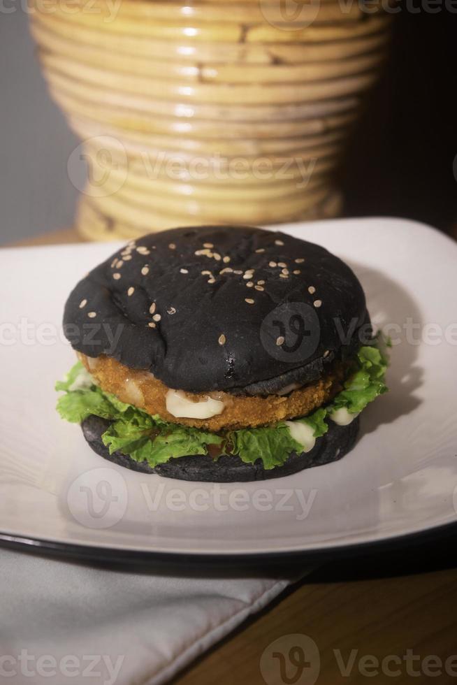Close up photo of the opened black burger on a white plate is highly suitable for a fast food menu