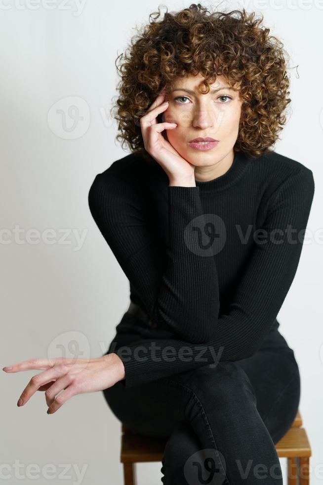 Focused curly haired woman sitting on wooden chair photo