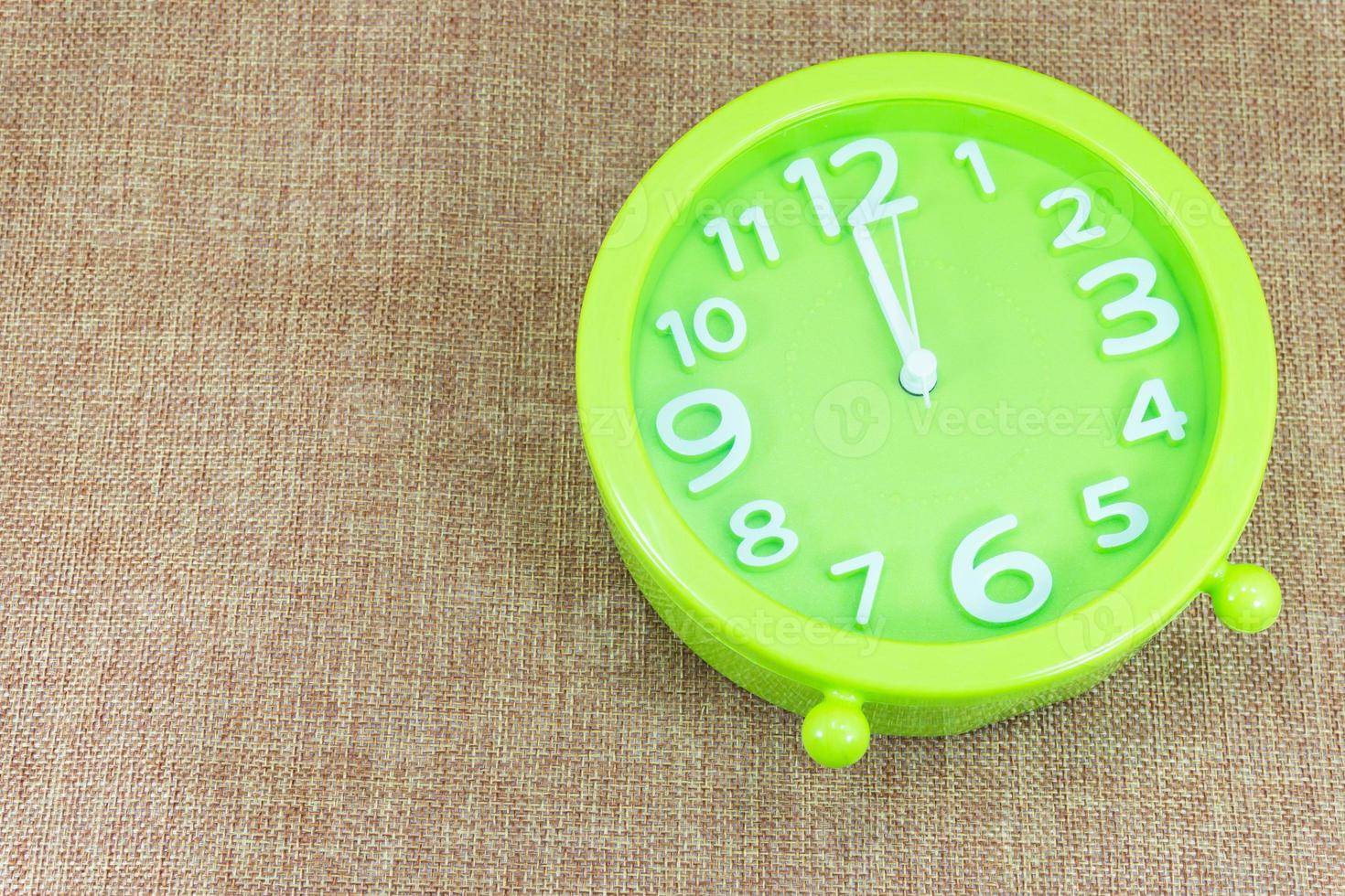 Green alarm clock on brown sackcloth background show 12.00 a.m. photo