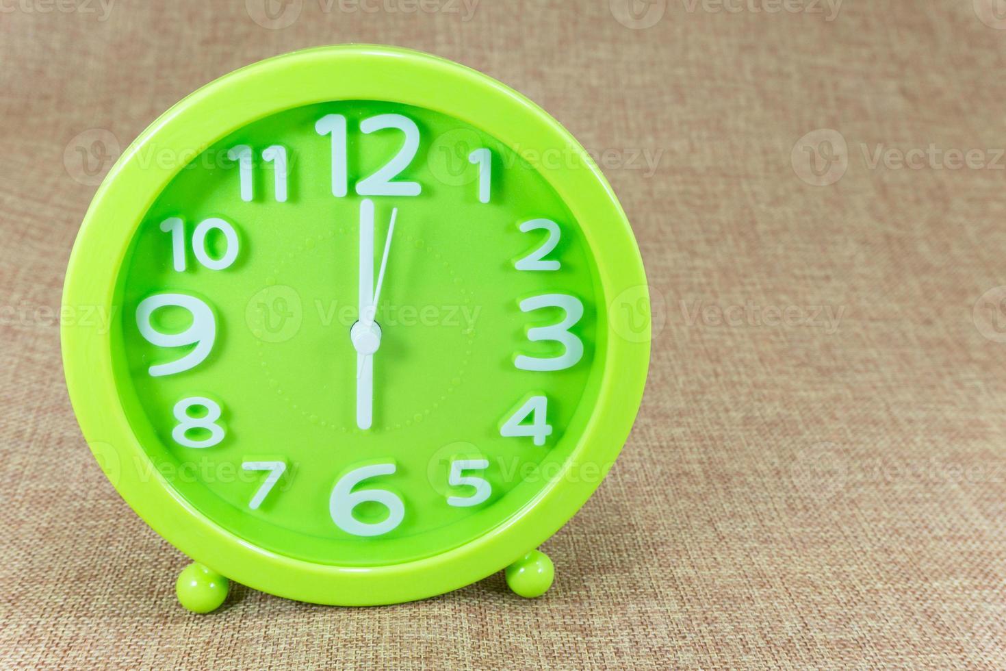 Green alarm clock on brown sackcloth background show Six o clock or 6.00 a.m. photo
