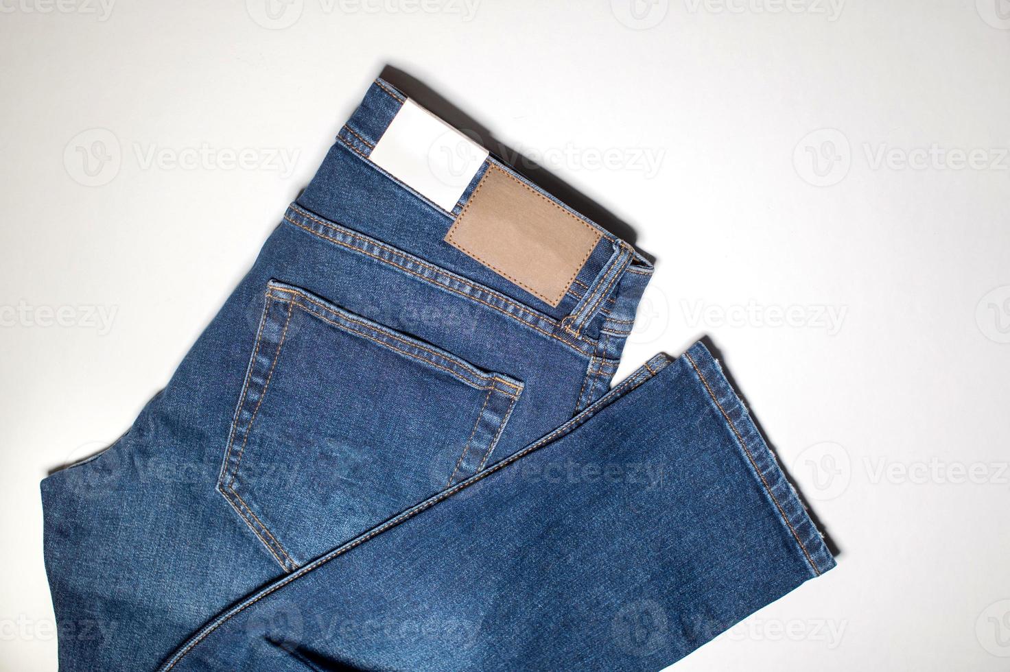 un par de mezclilla pantalones con un vacío cuero etiqueta mentira doblada en un blanco antecedentes. foto