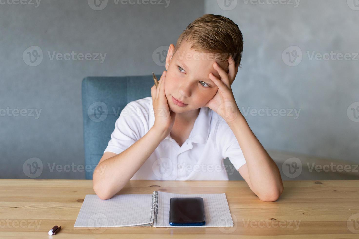 Cute boy writes in an open notebook and looks at the phone. photo
