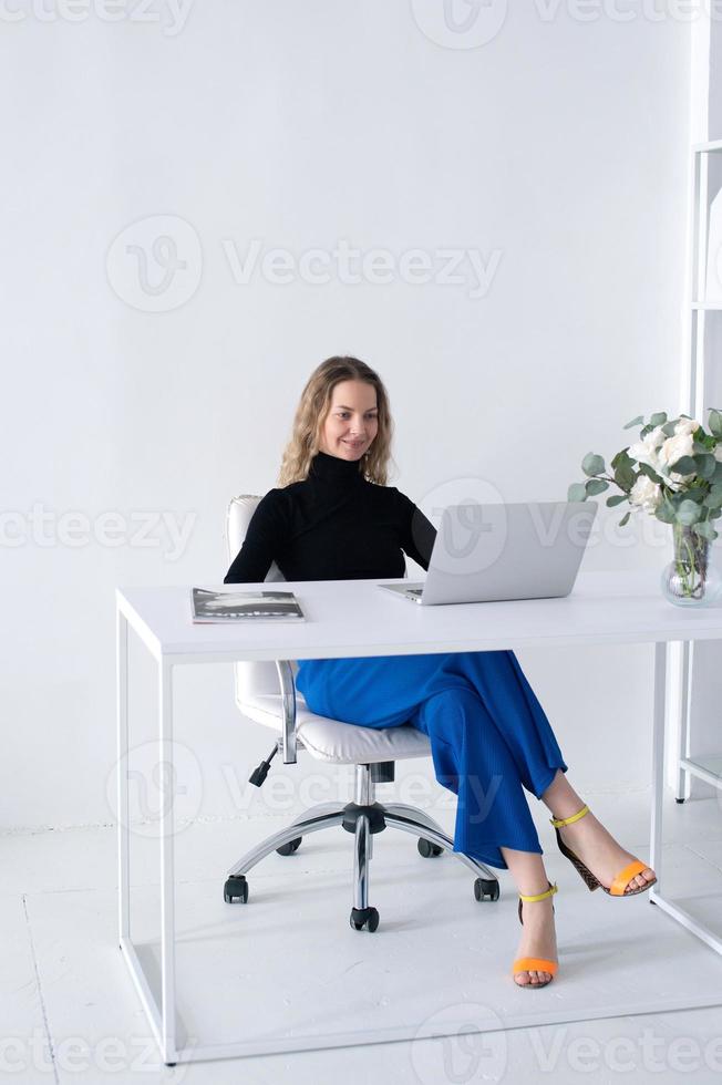 The girl works in a white office with a laptop and flowers on the table photo