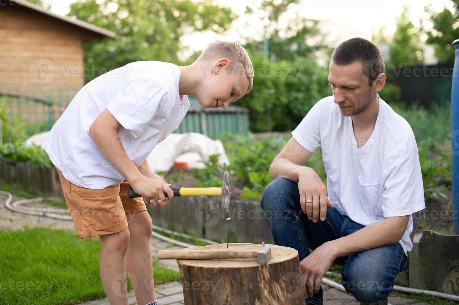 Dad teaches his son to hammer nails into a tree photo