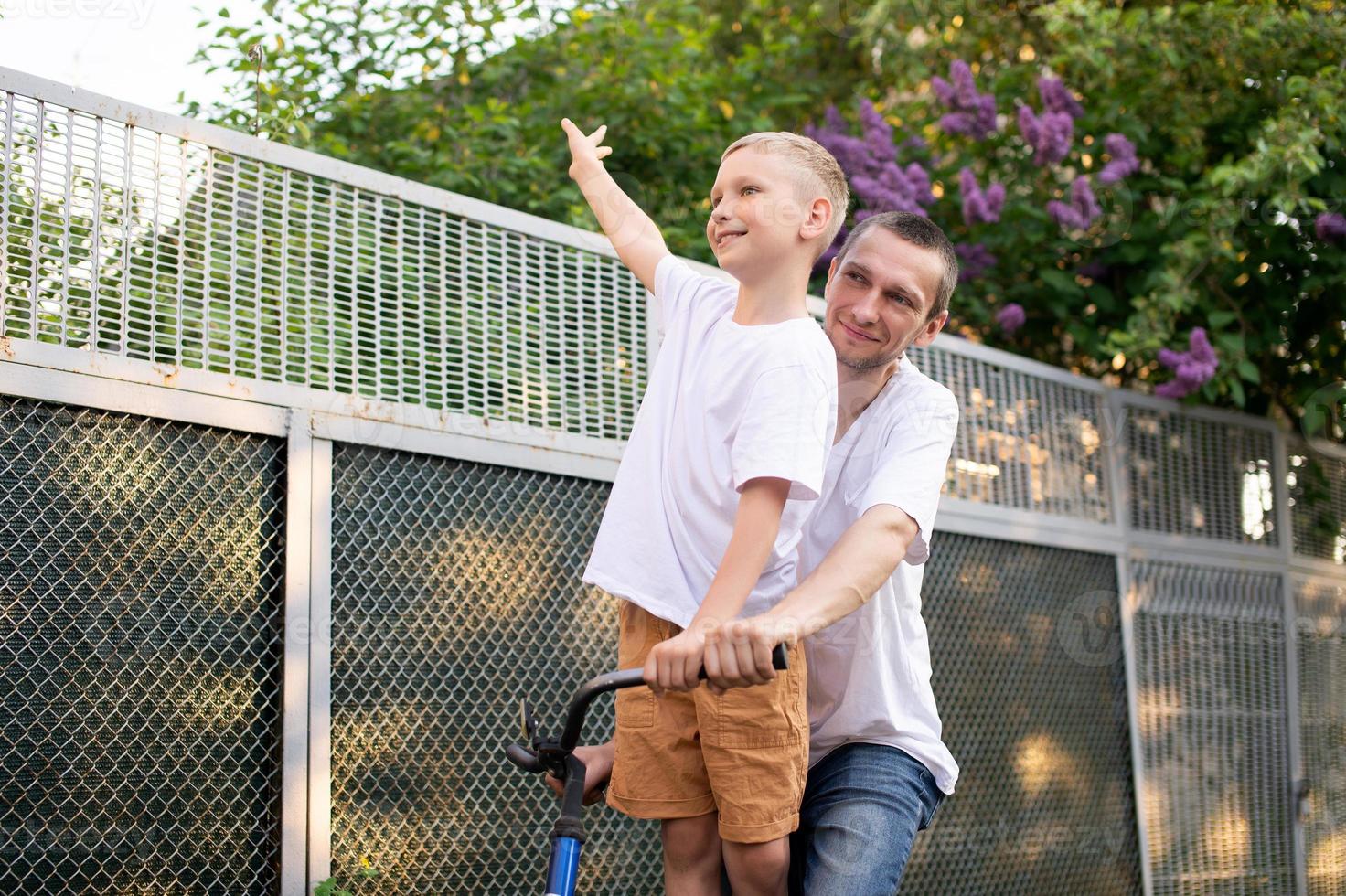 un linda chico en un blanco camiseta paseos un bicicleta con su papá y risas foto