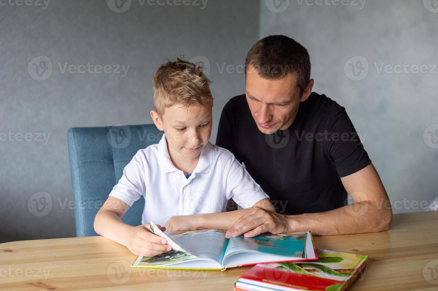 un linda chico es sentado a el mesa con su papá y acecho un libro acerca de serpientes foto