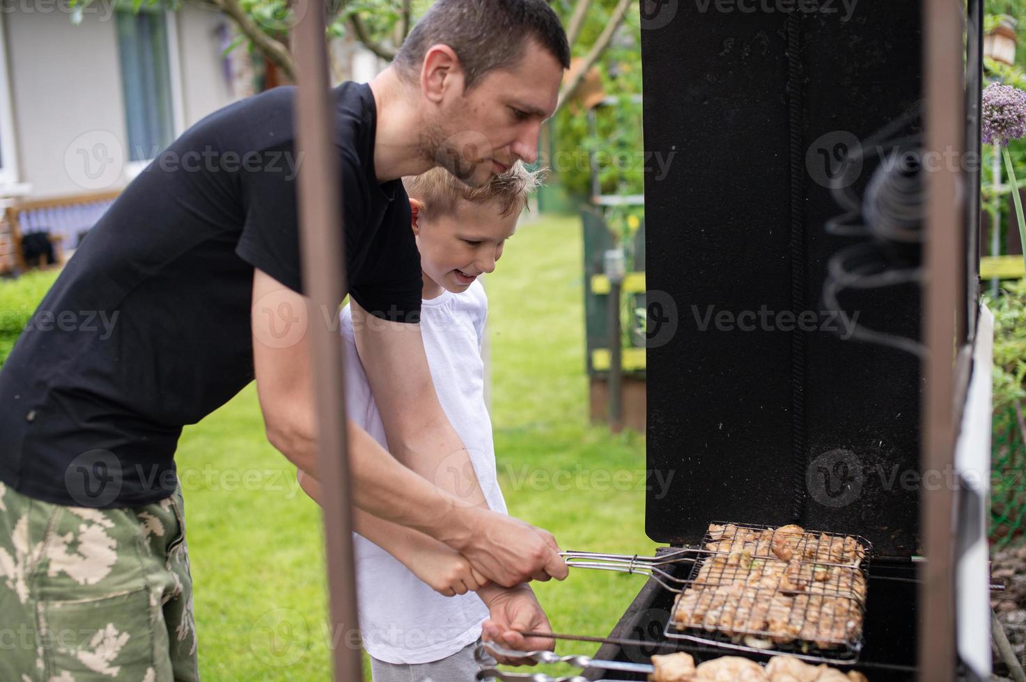 Cheerful dad and son roast meat on the grill photo