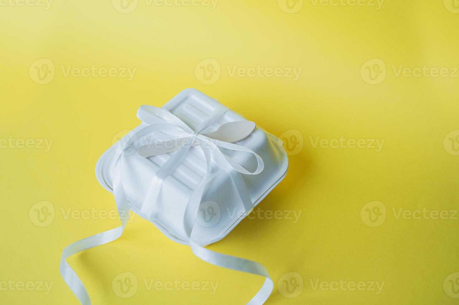 A bento cake box with a wooden spoon stands closed on a yellow background photo