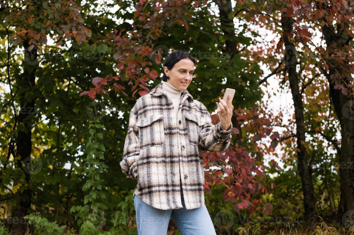 Cute girl has a video call on the phone against the background of an autumn forest photo