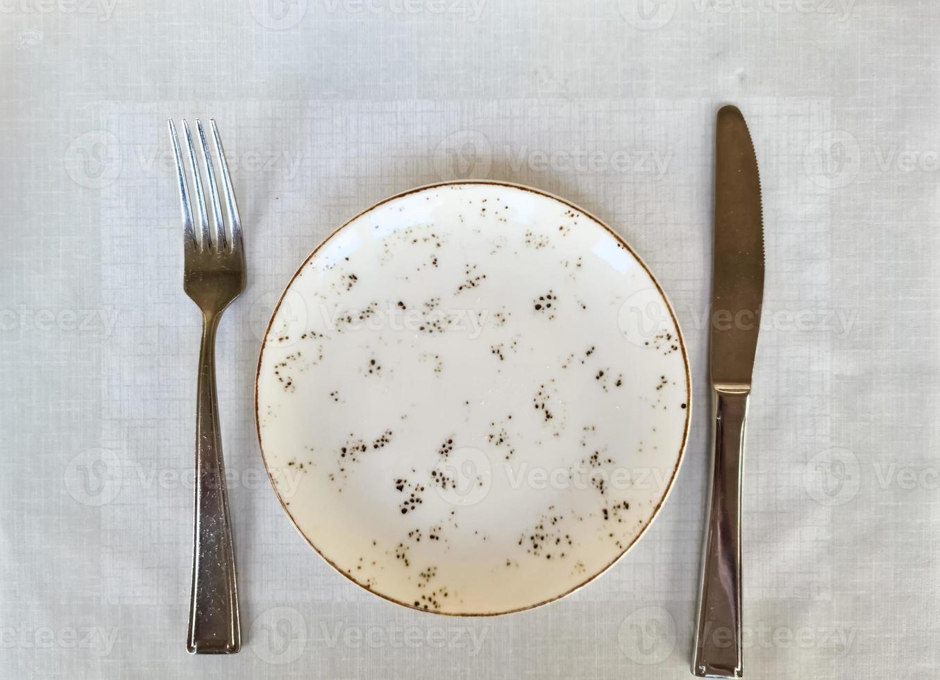 An empty light-coloured plate with knife and fork - view from above photo