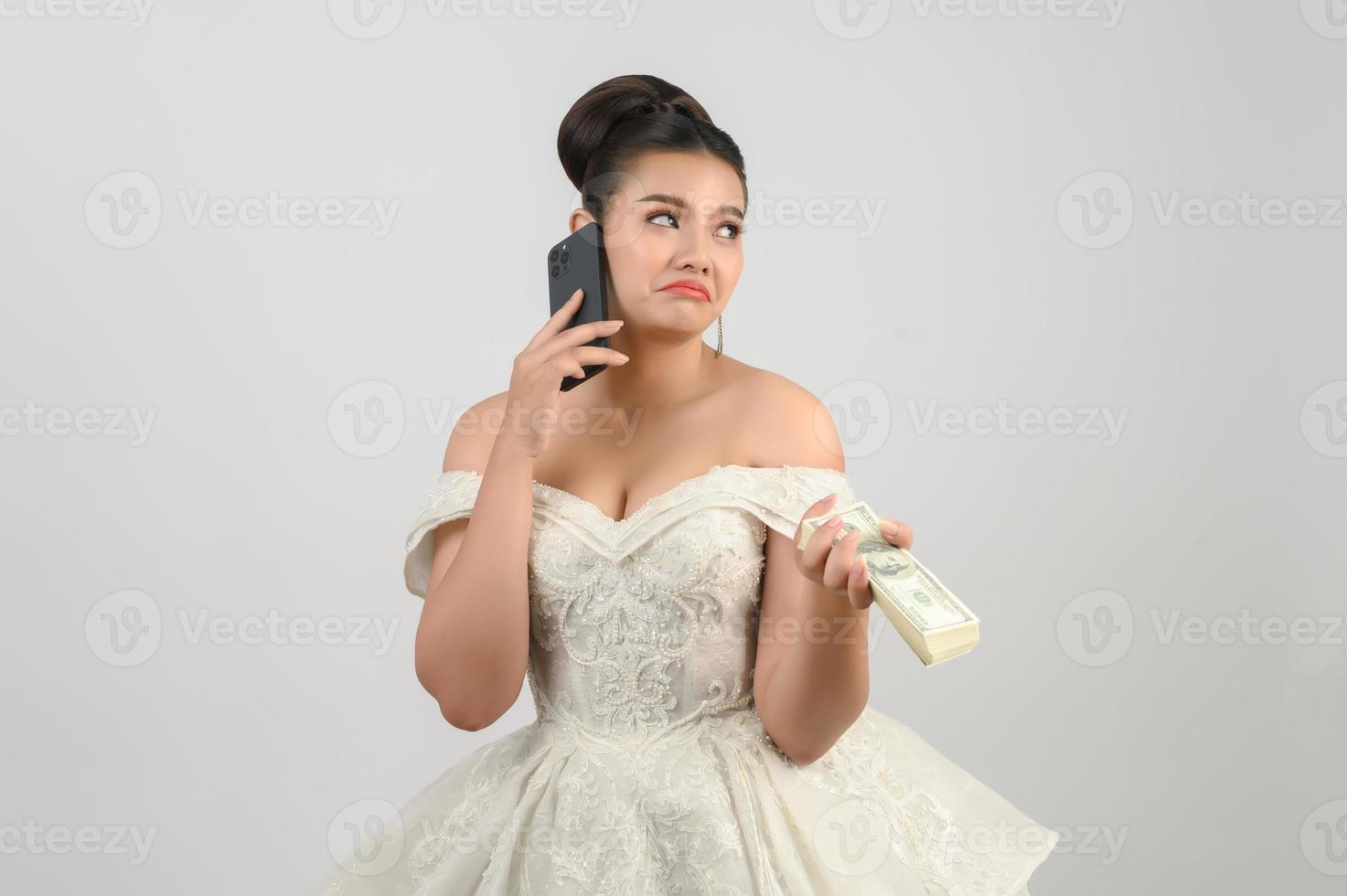 Young asian beautiful bride posting with smartphone and banknote in hand photo