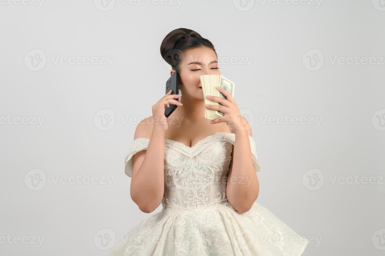 Young asian beautiful bride posting with smartphone and banknote in hand photo