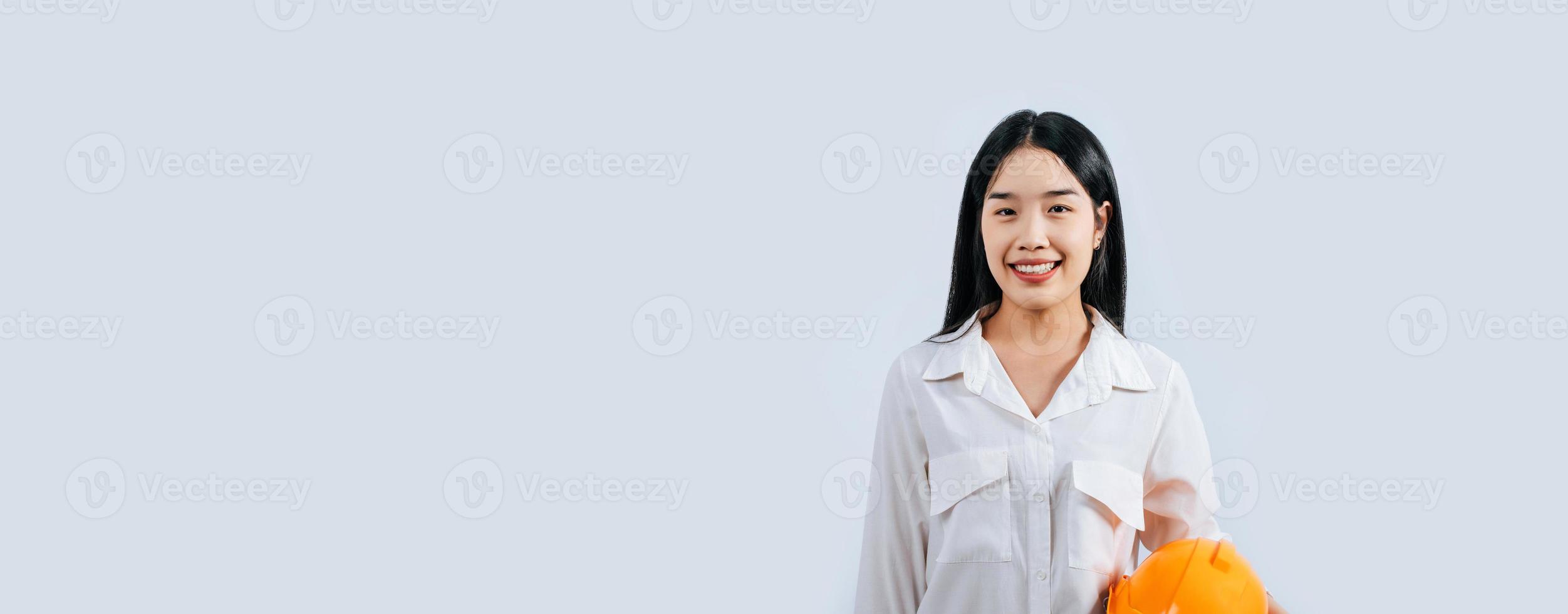 joven hembra ingeniero sostener amarillo casco estar con encantador sonrisa postura foto