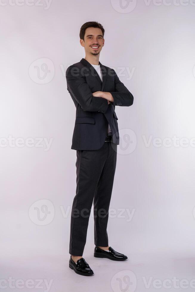 retrato de un joven apuesto hombre de negocios con traje de pie con los brazos cruzados aislado en el fondo blanco del estudio foto