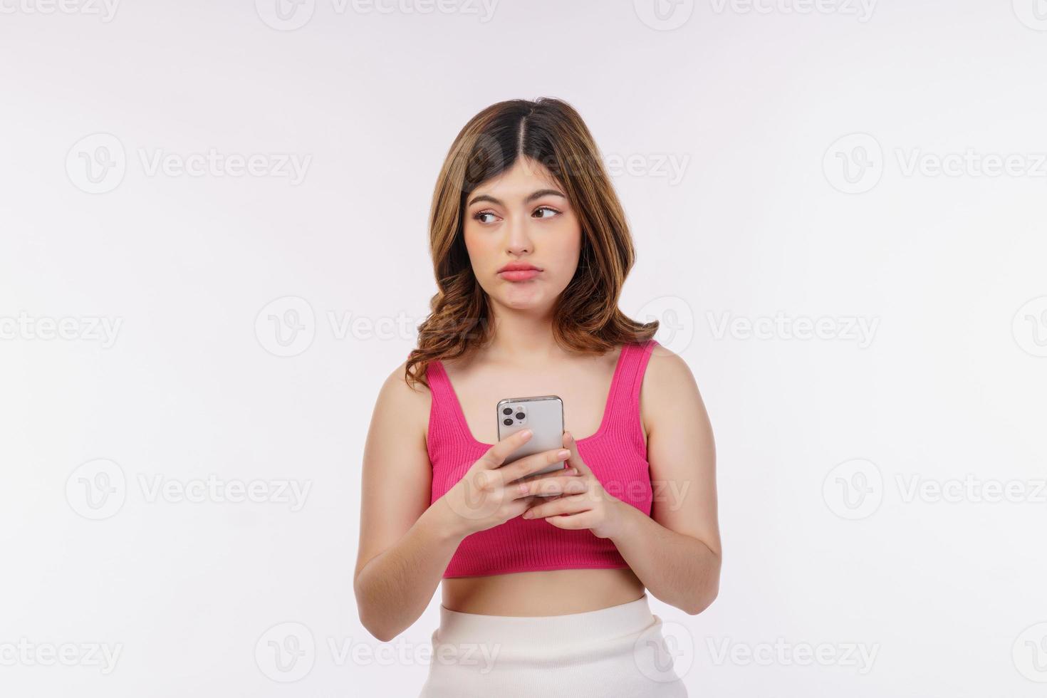 Retrato de mujer joven confundida a través de teléfono móvil aislado sobre fondo blanco. foto