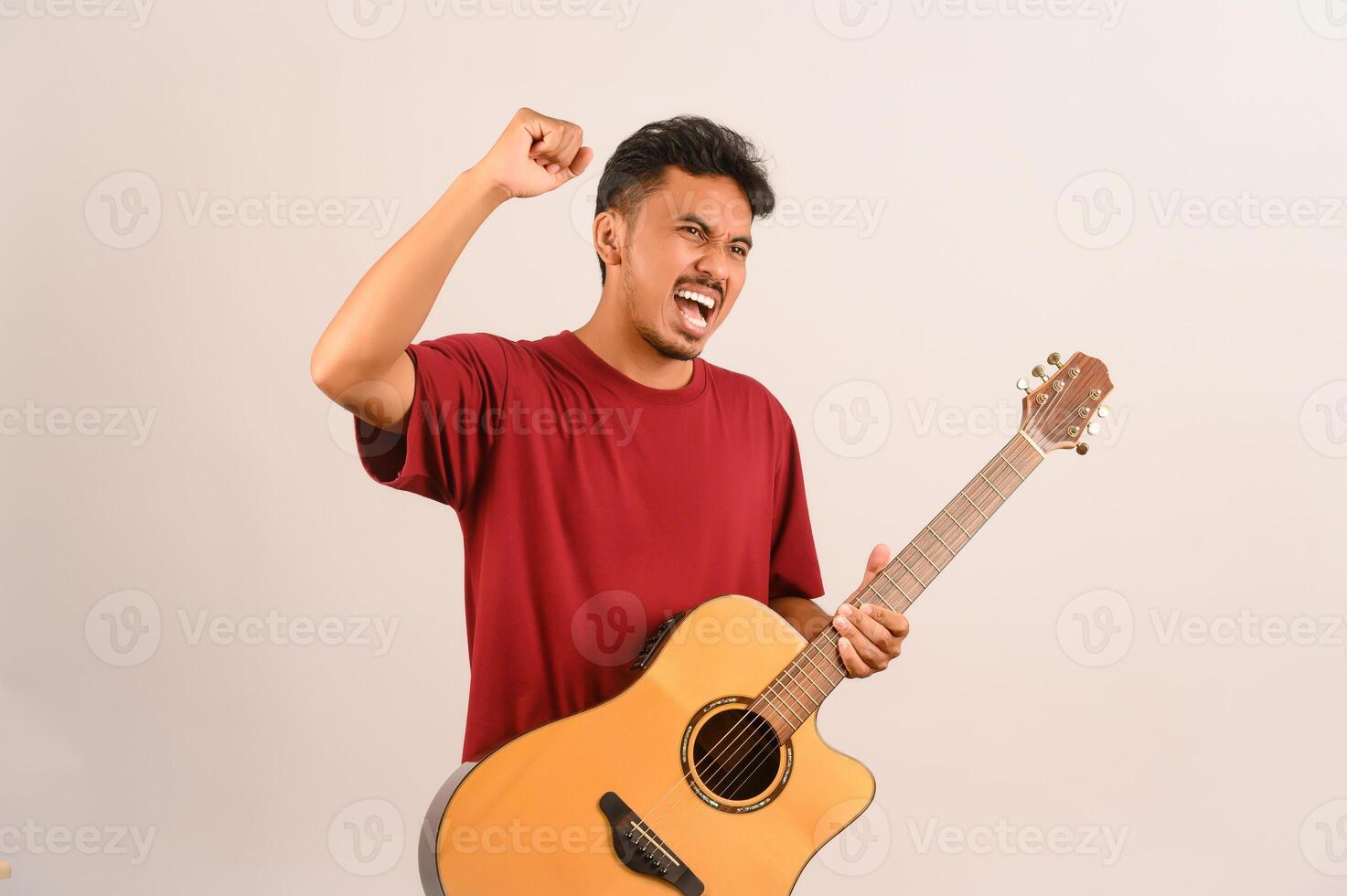 retrato de un joven asiático con una camiseta roja con una guitarra acústica aislada de fondo blanco foto