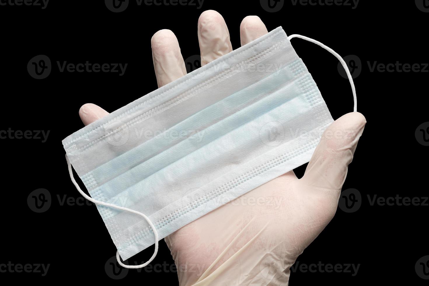 Doctor holds face mask in hand in white medical gloves isolated on black background. Concept coronavirus quarantine photo