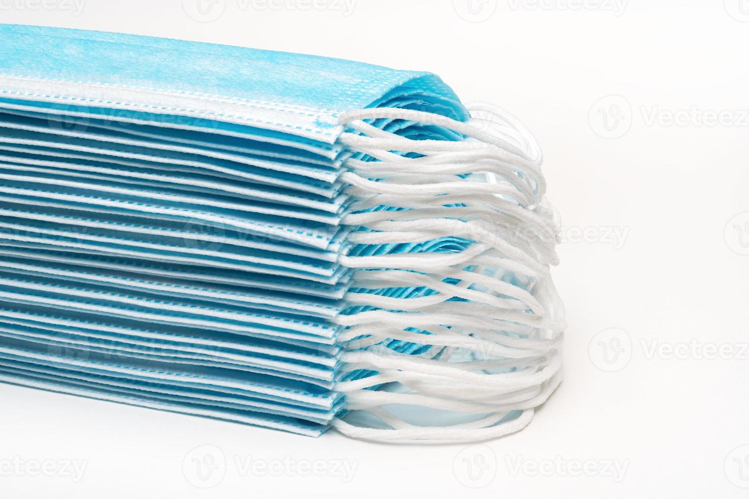 Stack blue surgical medical face masks with rubber ear straps on white background. Close-up view, forced perspective photo