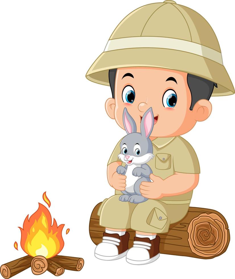 an adventurous boy sits on a fallen tree and holds a rabbit while lighting a bonfire vector