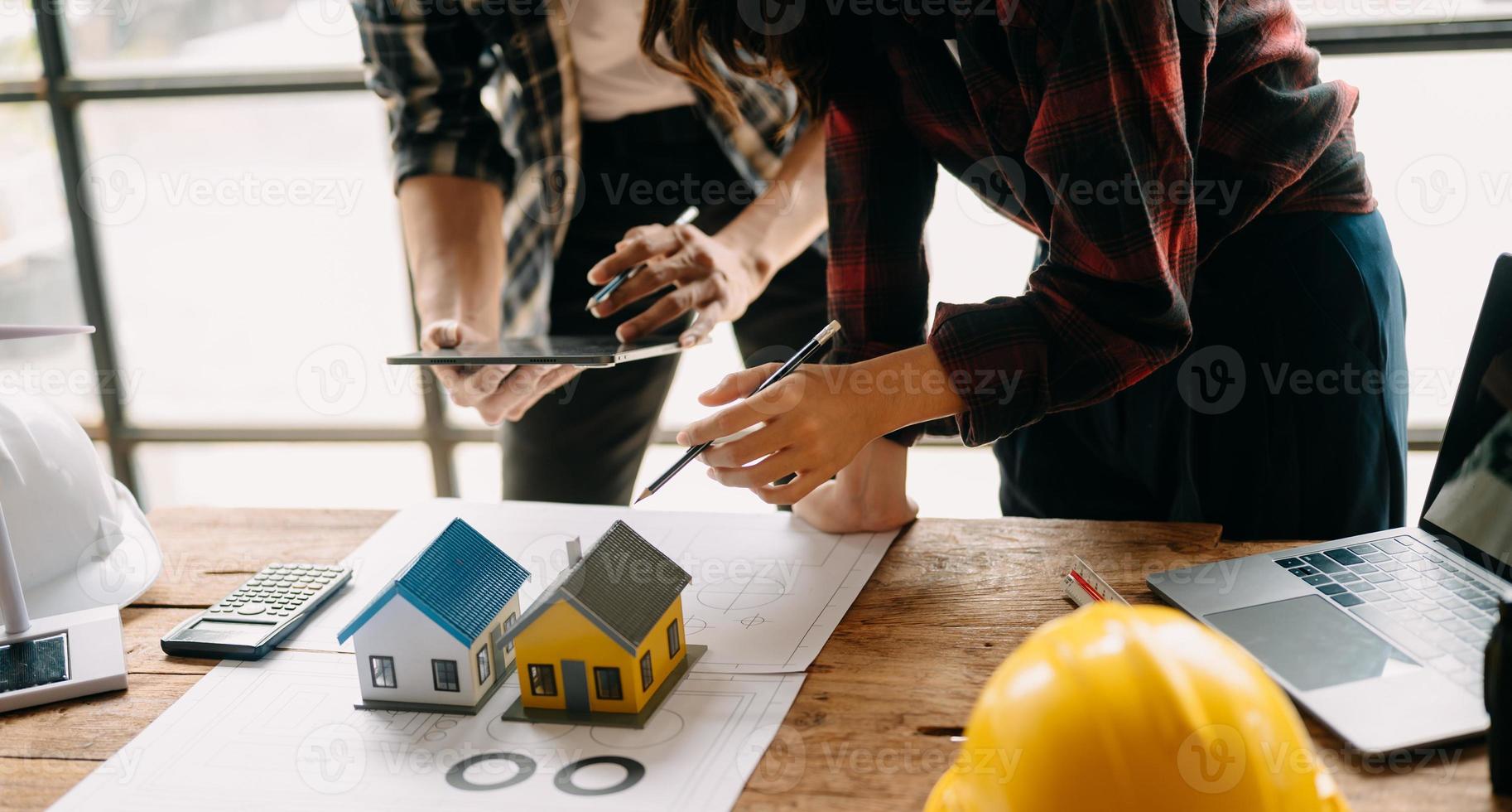 Dos colegas discutiendo el trabajo de datos y una tableta, un portátil con un proyecto arquitectónico en el sitio de construcción en un escritorio en la oficina foto