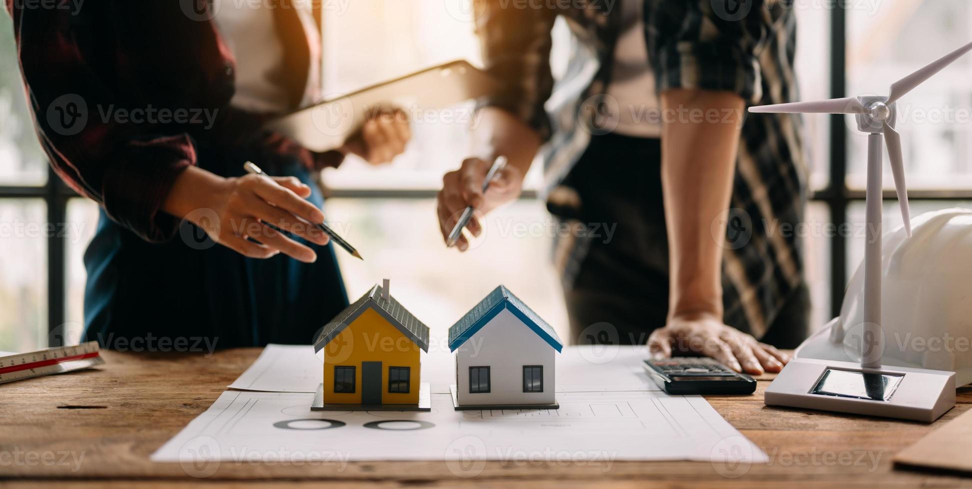 Dos colegas discutiendo el trabajo de datos y una tableta, un portátil con un proyecto arquitectónico en el sitio de construcción en un escritorio en la oficina foto