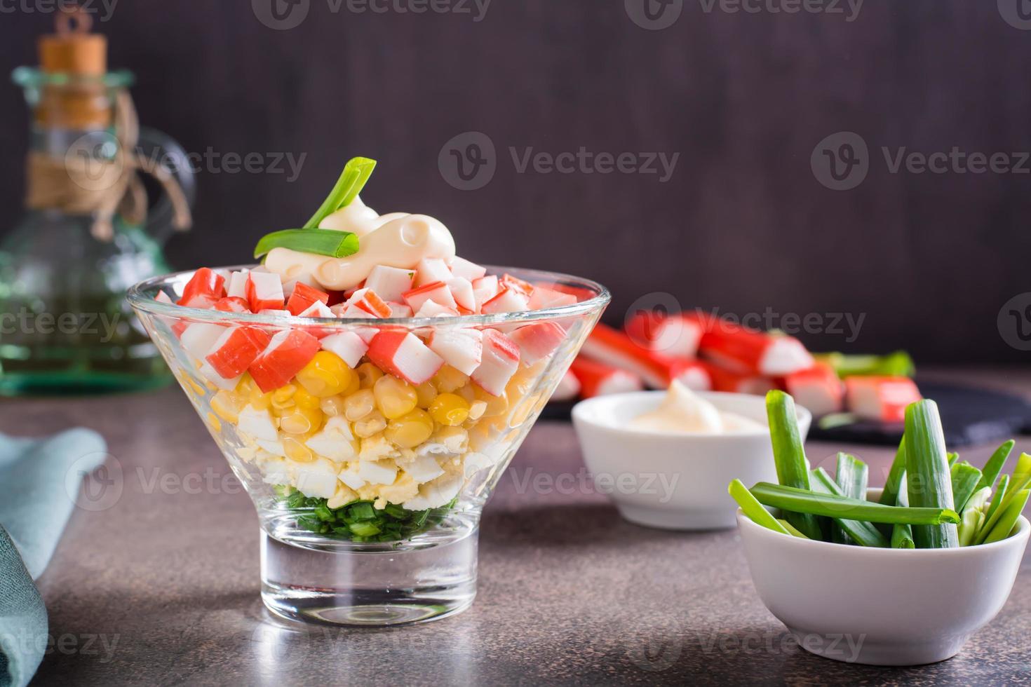 Crab salad of fish sticks, eggs, onions and corn in a bowl on the table photo