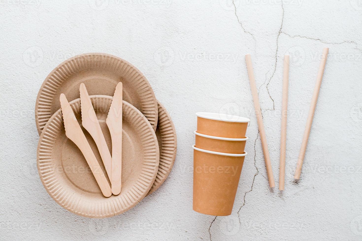 Eco friendly disposable cardboard tableware. Plates, cups and tubes, and wooden knives on a light background. Top view. photo