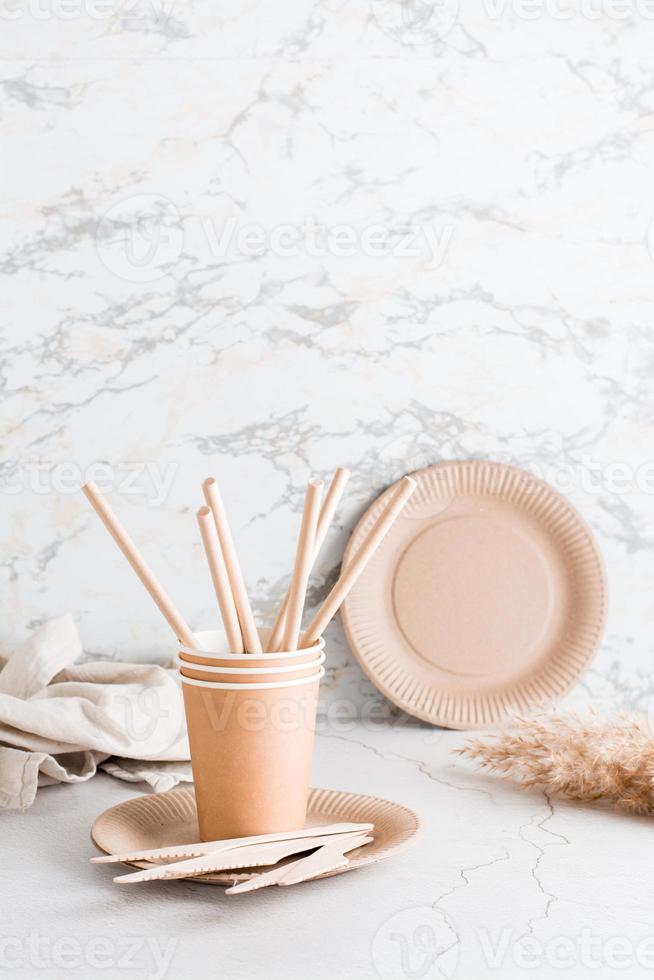 Eco friendly disposable cardboard tableware. Plates, cups and pipes and wooden knives on the table. Vertical view photo
