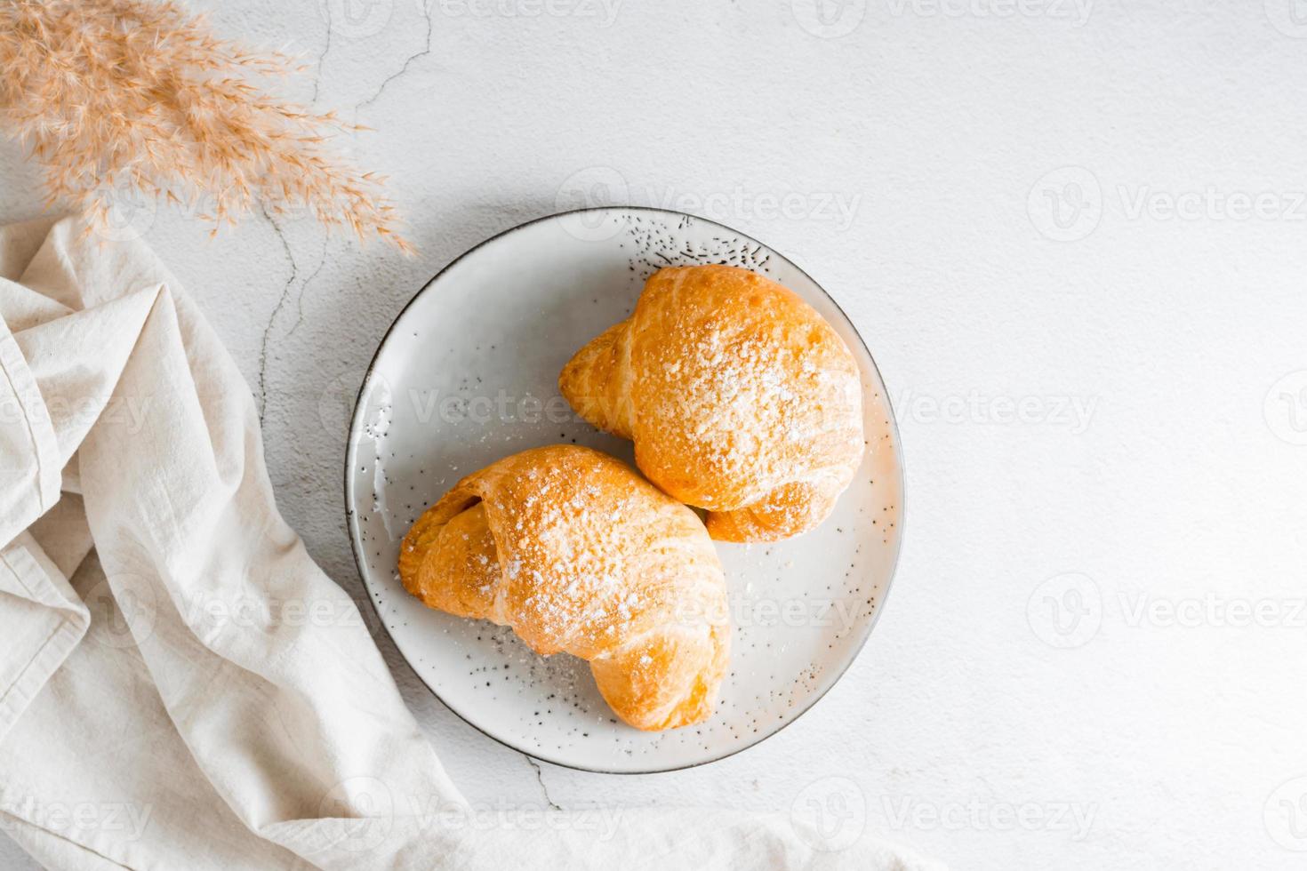 A couple of fresh croissants on a plate on the table. Lifestyle homemade snack. Top view. photo