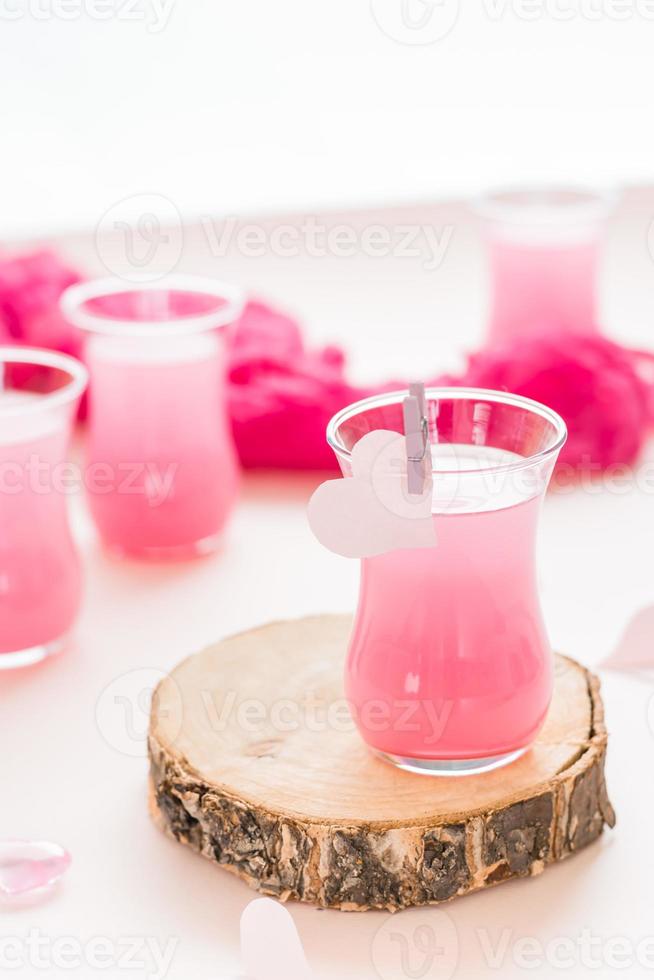 Pink cocktail in a glass on a tree trunk and paper hearts on a pink background. Drinks for lovers. Vertical view photo