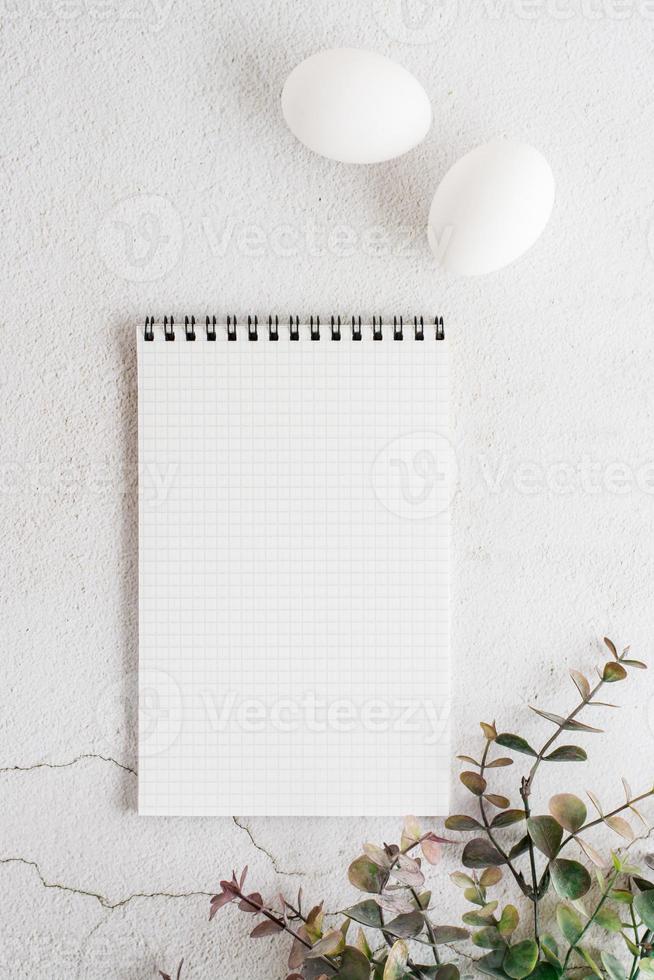 Notepad for writing, white eggs and eucalyptus branch on a light textured background. Happy eco easter invitation. Top and vertical view. photo