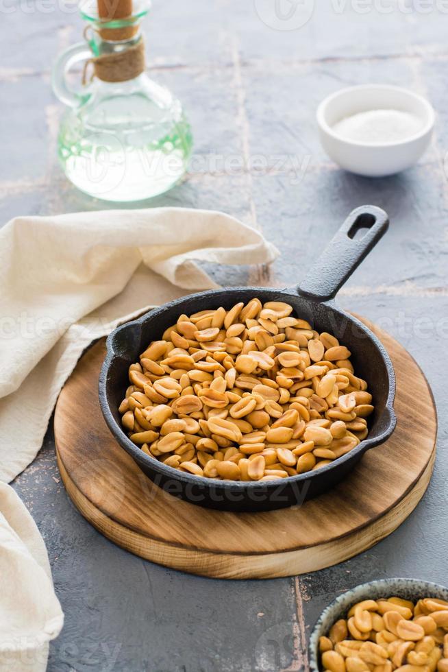 Fresh roasted peanuts in a frying pan, salt and oil on the table. Plant source of protein. Vegetarian food. Vertical view photo