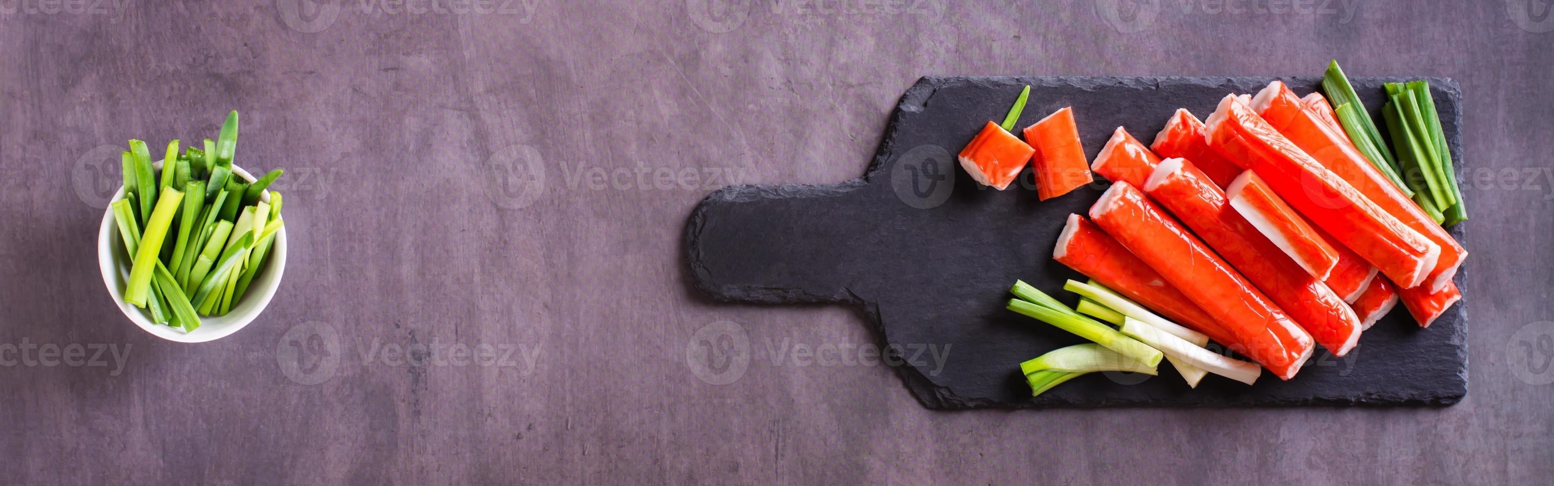 Crab sticks and chives on a stone board and sauce in a bowl. Top  view. Web banner photo