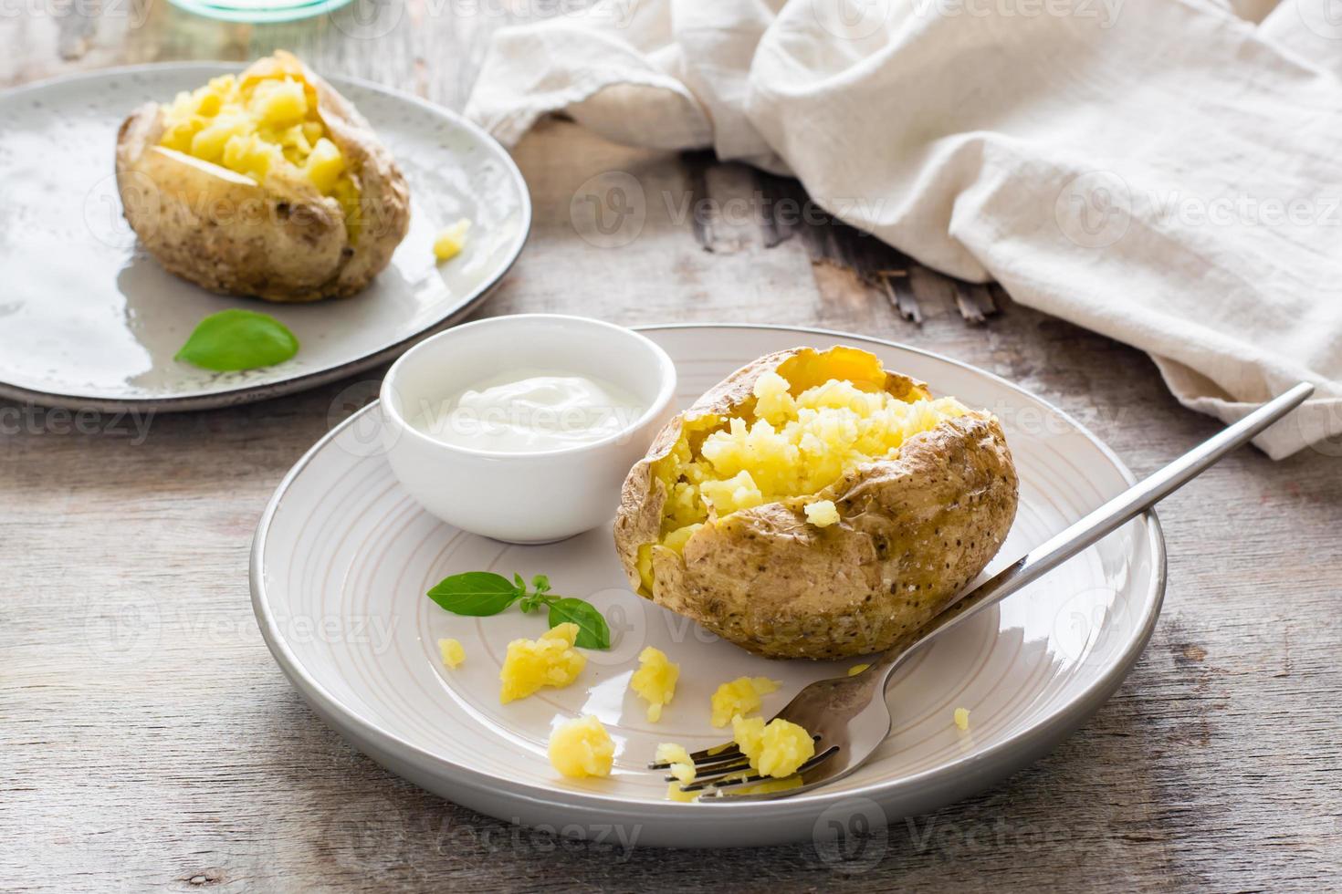 Baked potatoes in their skins and a bowl of sour cream on a plate on a wooden table. Vegetarian natural food photo