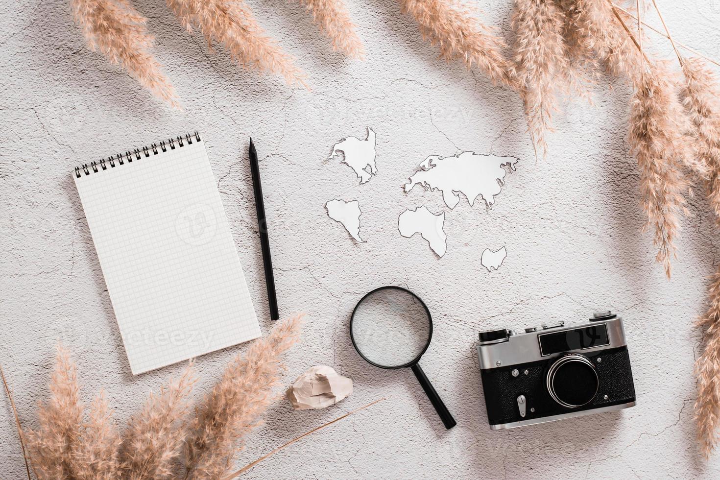 Flat lay concept travel. Notebook, pencil, continent templates, magnifier and vintage camera surrounded by grass on textured concrete background. photo