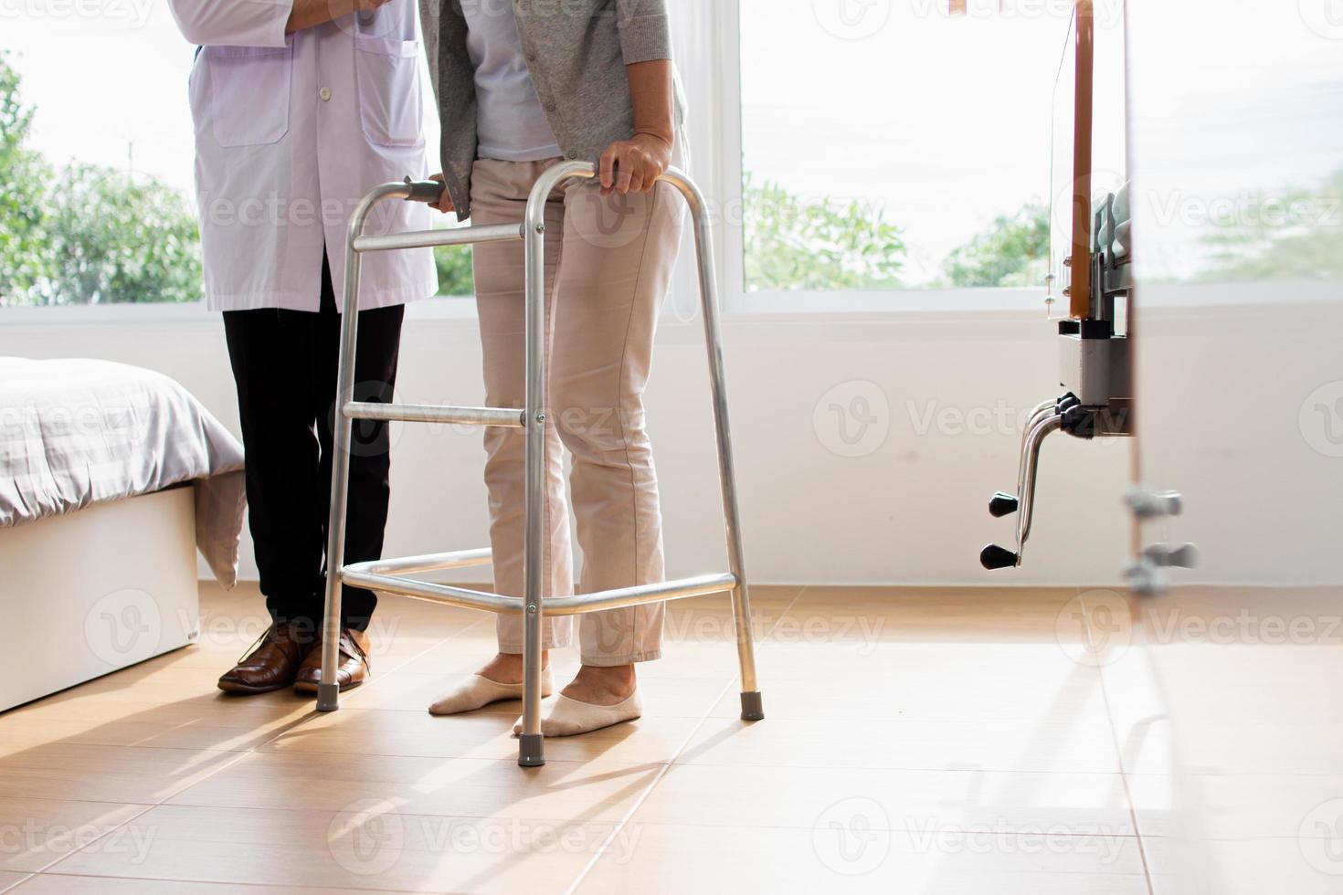 caucásico masculino médico Ayudar hembra paciente tratar a caminar con caminante. médico es examinando el paciente en el hospital. foto