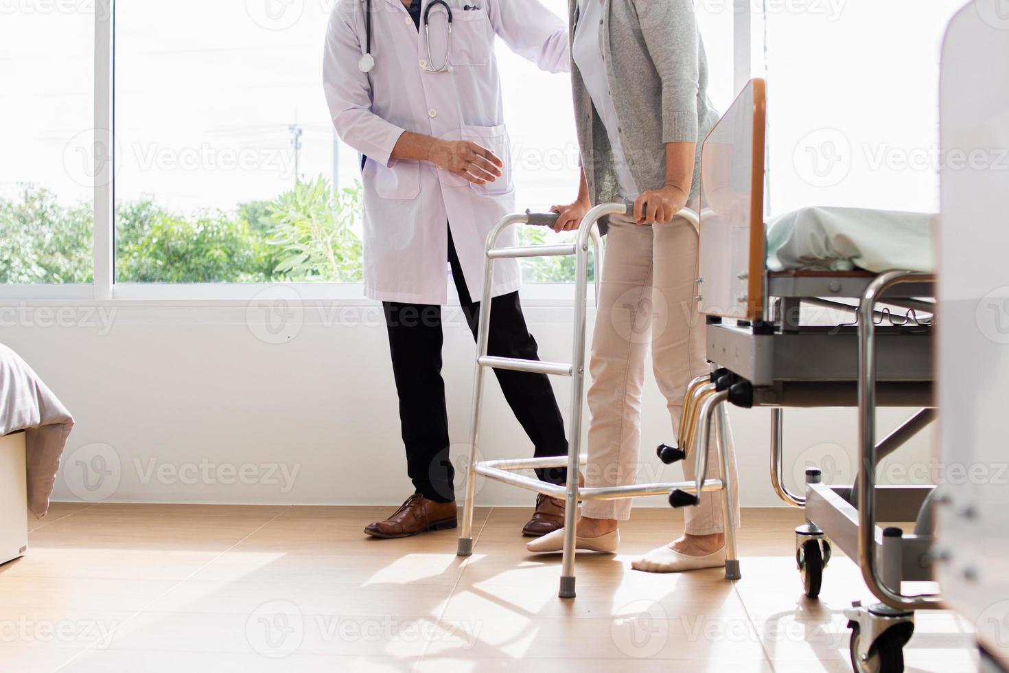 Caucasian male doctor helping female patient try to walk with walker. Doctor is examining the patient in the hospital. photo