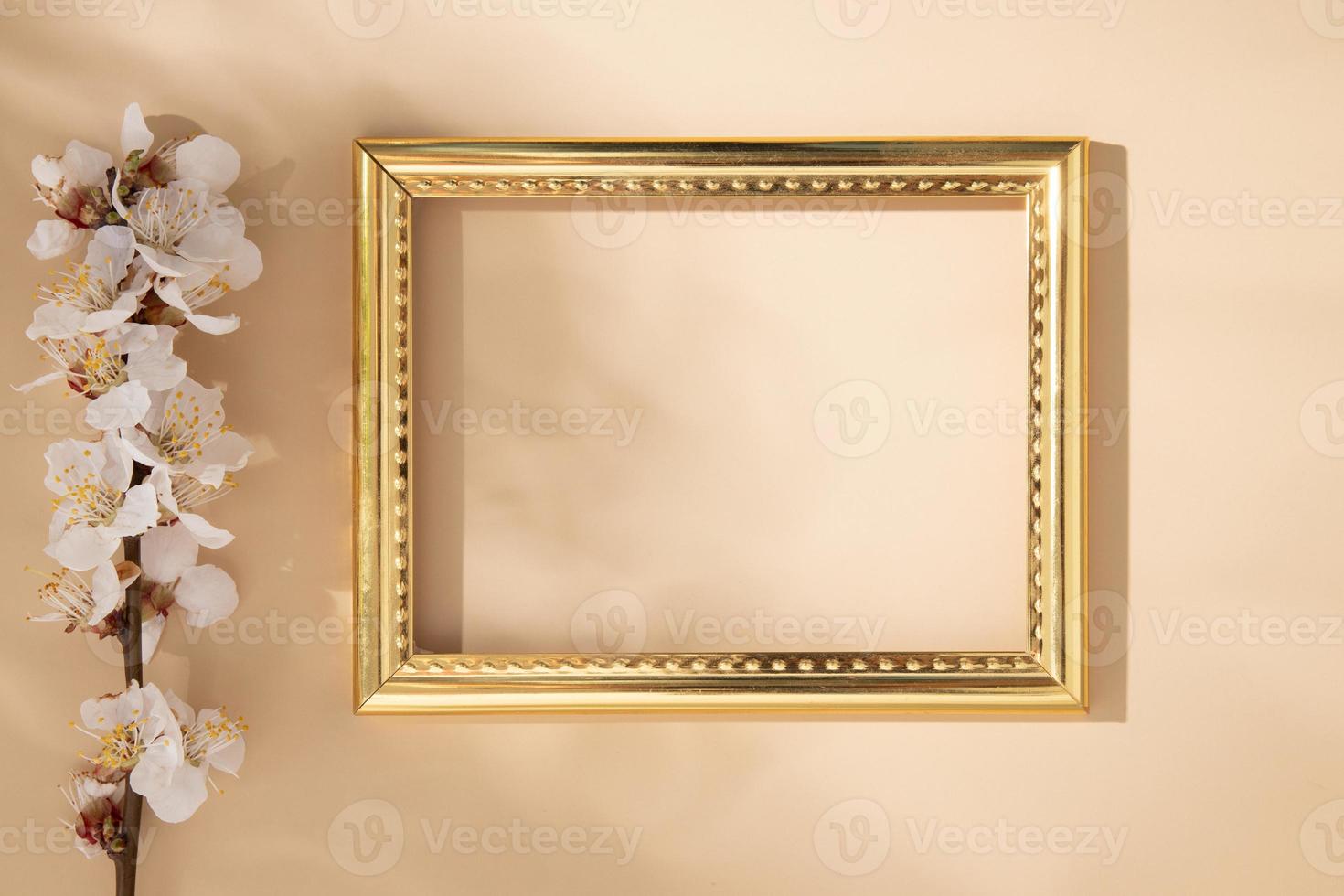 Empty golden frame with delicate cherry petals on a beige background photo