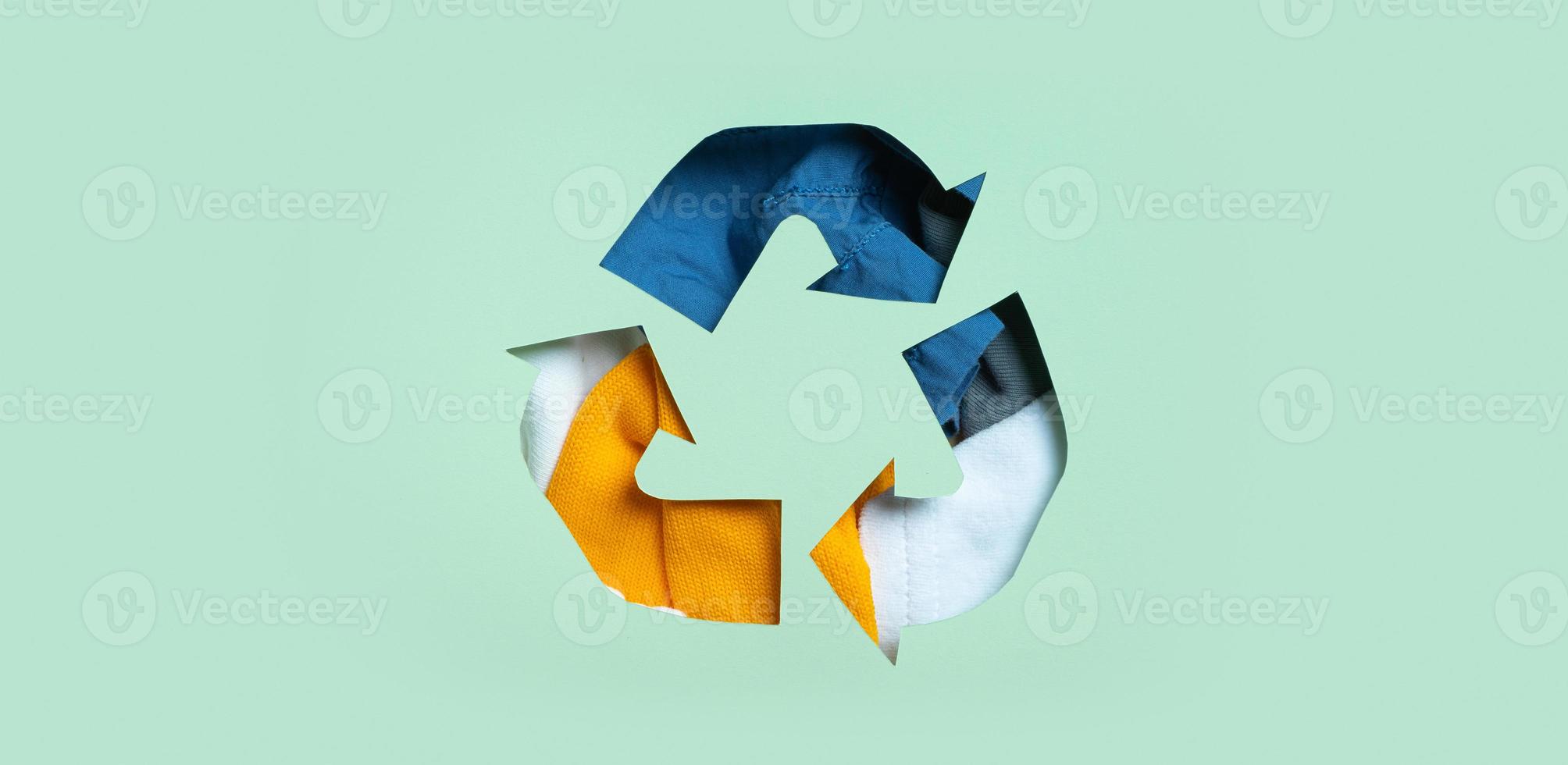 Second hand, clothing donation and recycling concept. Colorful clothes under paper cut recycling symbol photo