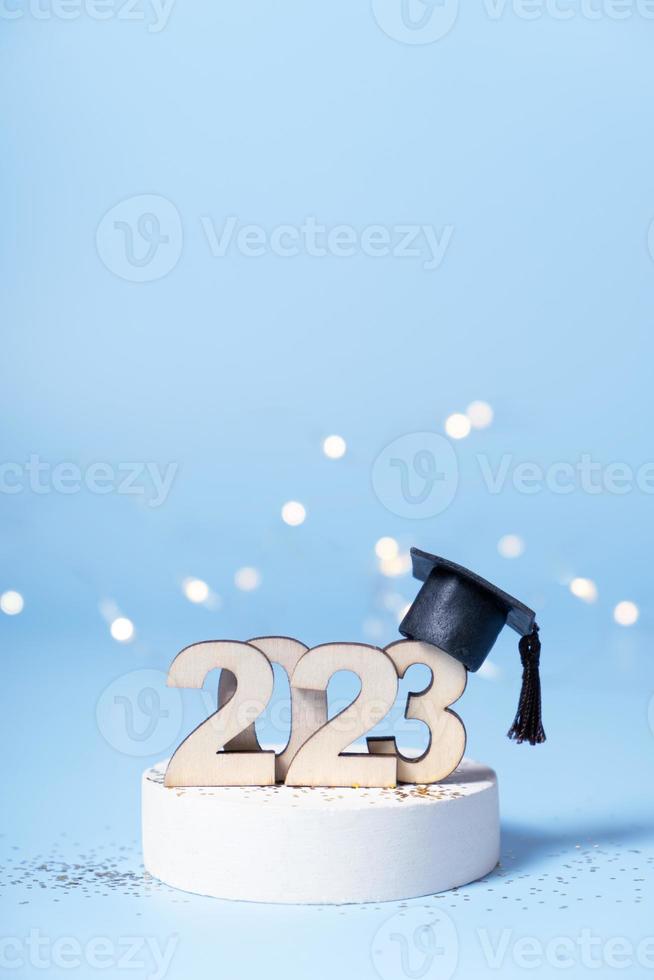 Class of 2023 concept. Wooden number 2023 with graduated cap on podium on colored background photo