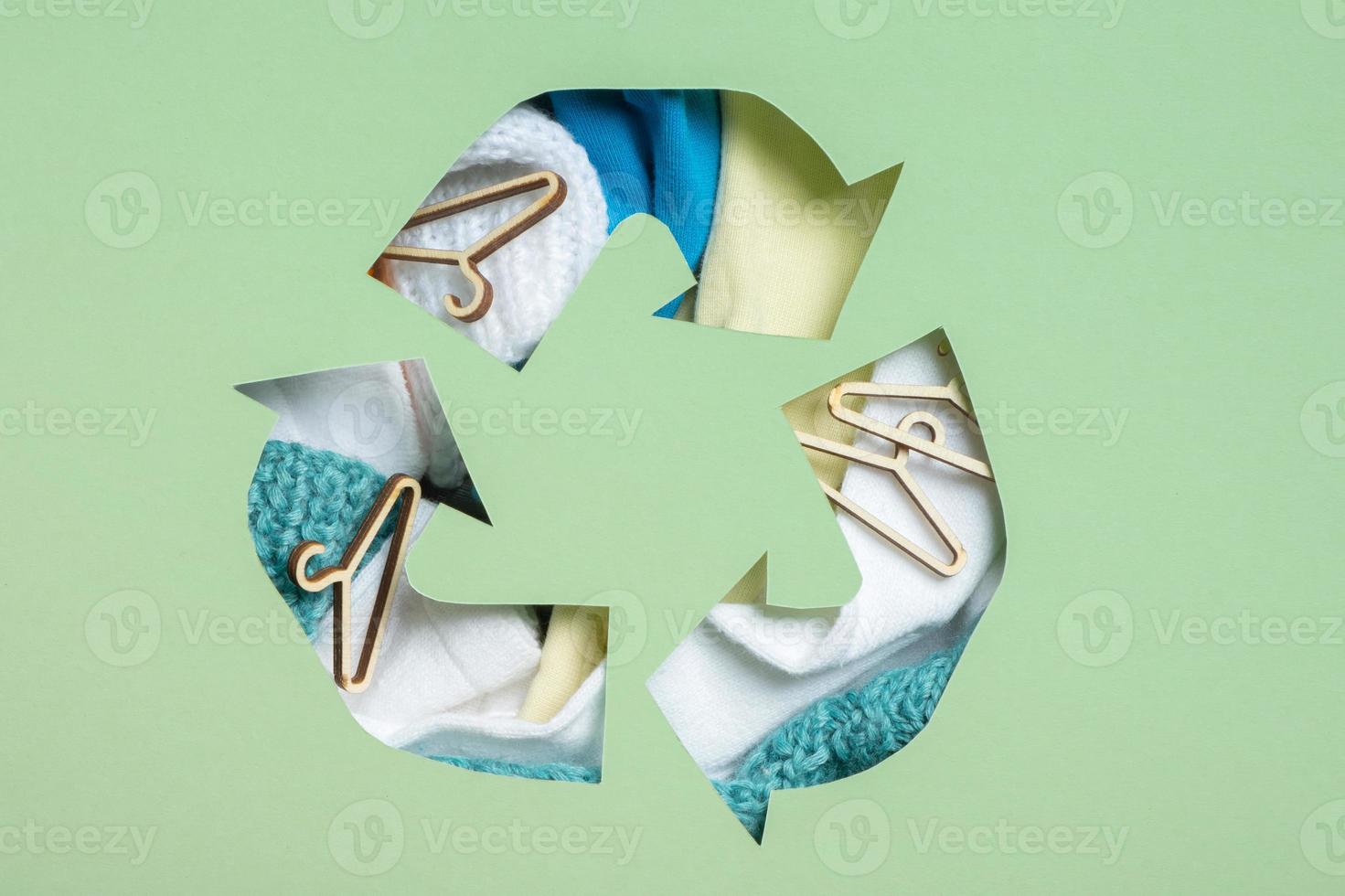 Colorful clothes and mini hungers under paper cut recycling symbol. Second hand, clothing donation and recycling concept photo
