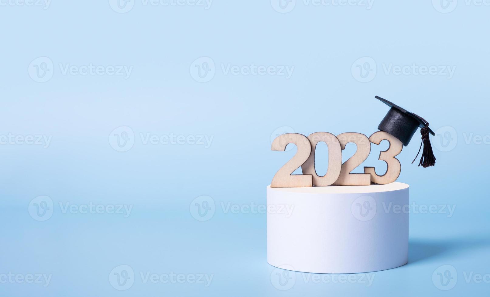 Class of 2023 concept. Wooden number 2023 with graduated cap on podium on colored background photo
