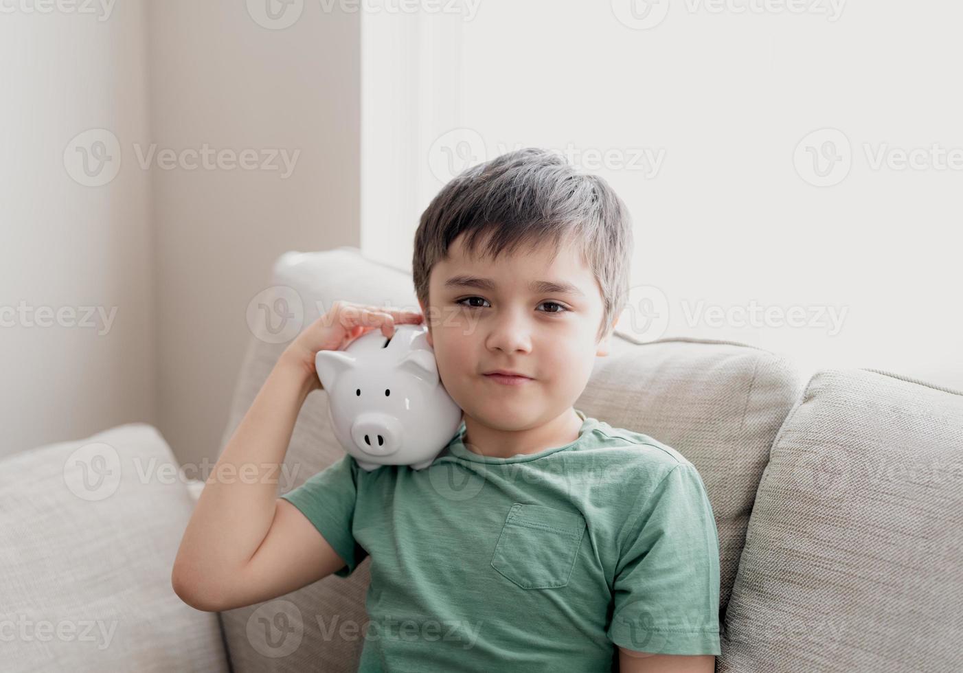 Happy boy holding piggy bank with smiling face. Indoor portrait of a cheerful child showing money saving box.School kid Learning financial responsibility and planning about saving for future concept photo