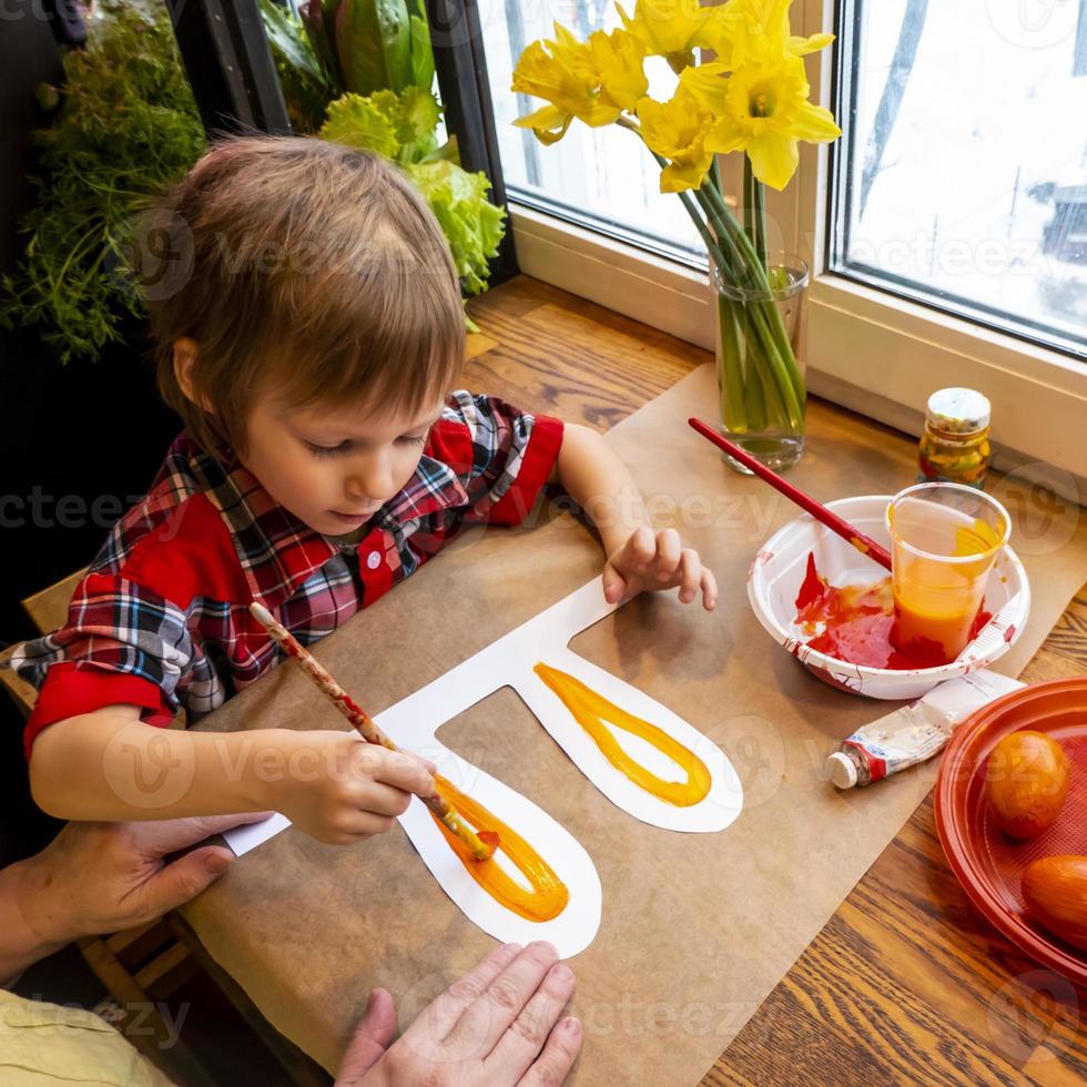 boy drawing the ears of a handmade Easter bunny made of cardboard. Preparation for the celebration of the Easter holiday. photo