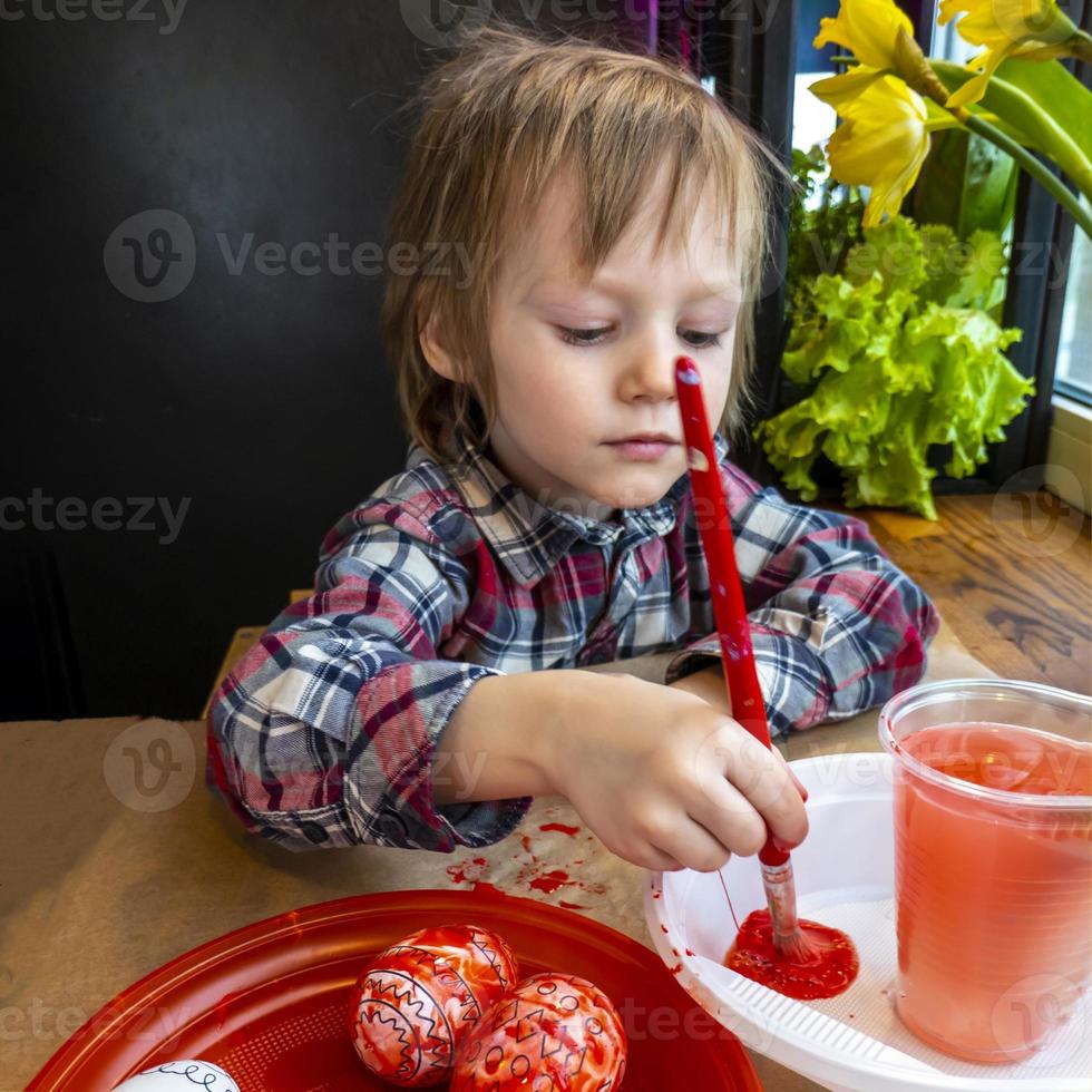 The child preparing for Easter. Paint eggs. Red paint egg. photo
