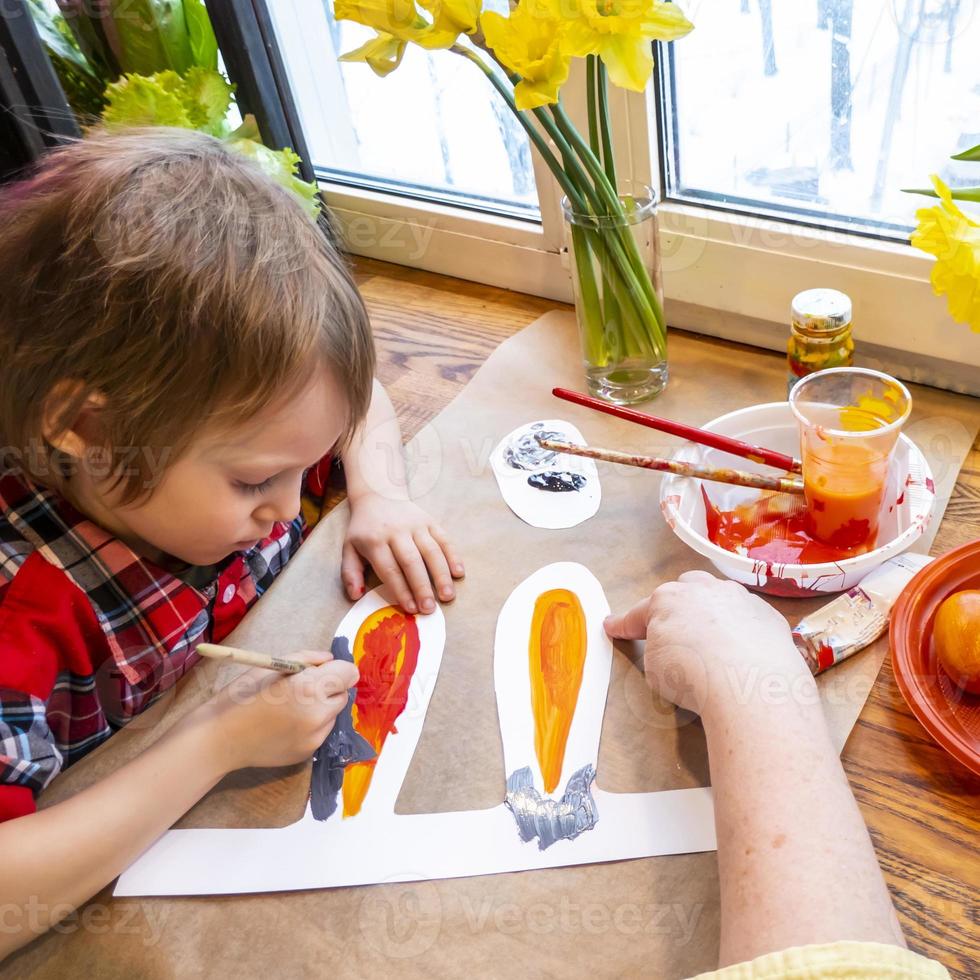 women's speckled hands teach boy drawing the ears of a handmade Easter bunny made of cardboard. Preparation for the celebration of the Easter holiday. photo