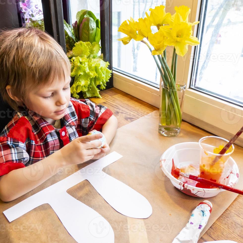 boy drawing the ears of a handmade Easter bunny made of cardboard. Preparation for the celebration of the Easter holiday. photo