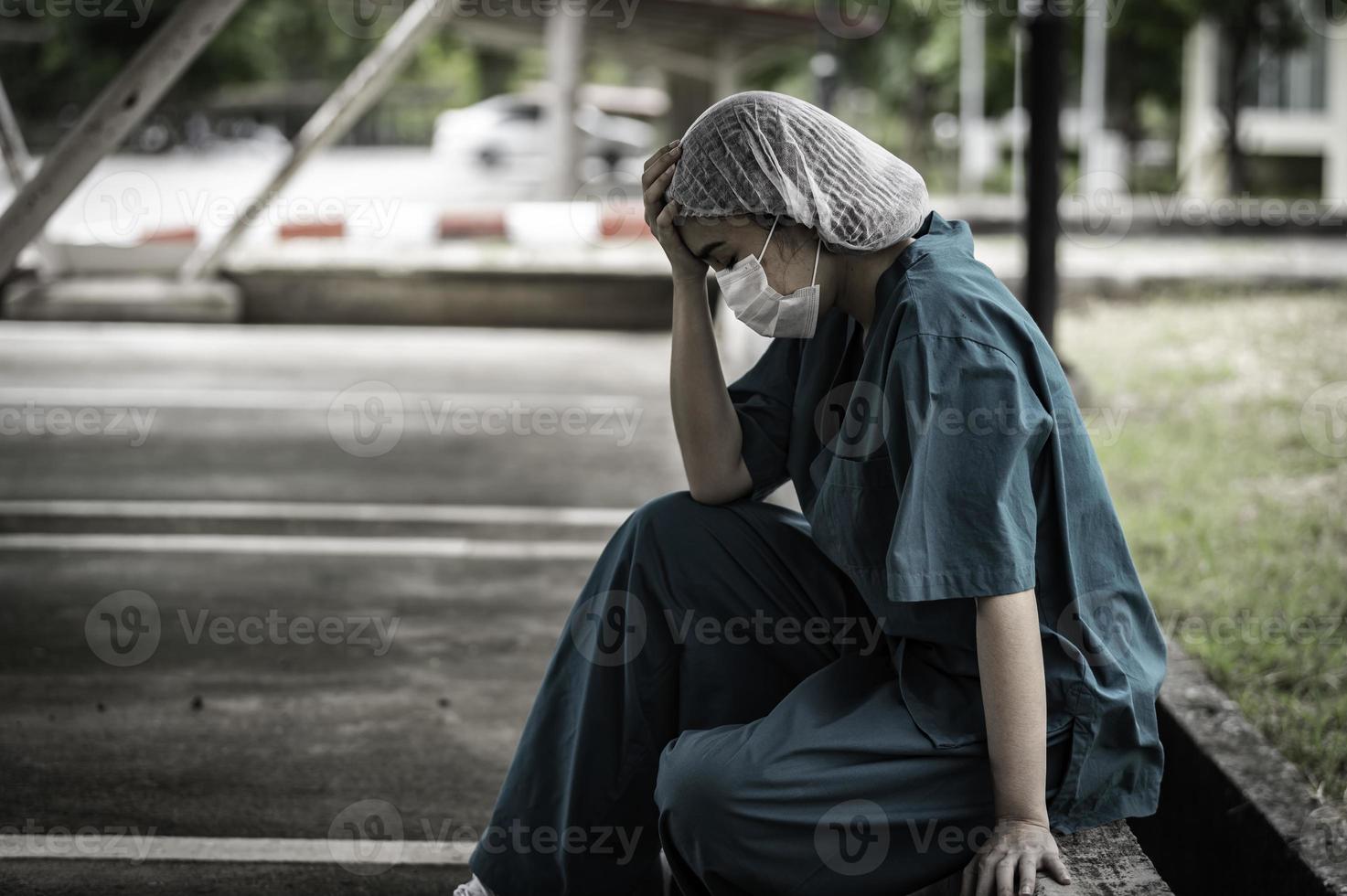 una enfermera asiática cansada y deprimida usa una máscara facial uniforme azul sentada en el piso del hospital, una joven doctora estresada por el trabajo duro foto