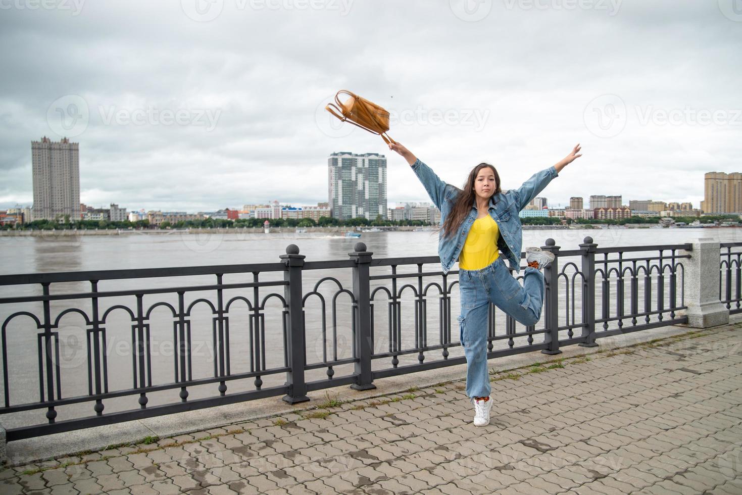 chica feliz con ropa de mezclilla saltando con mochila en la mano foto